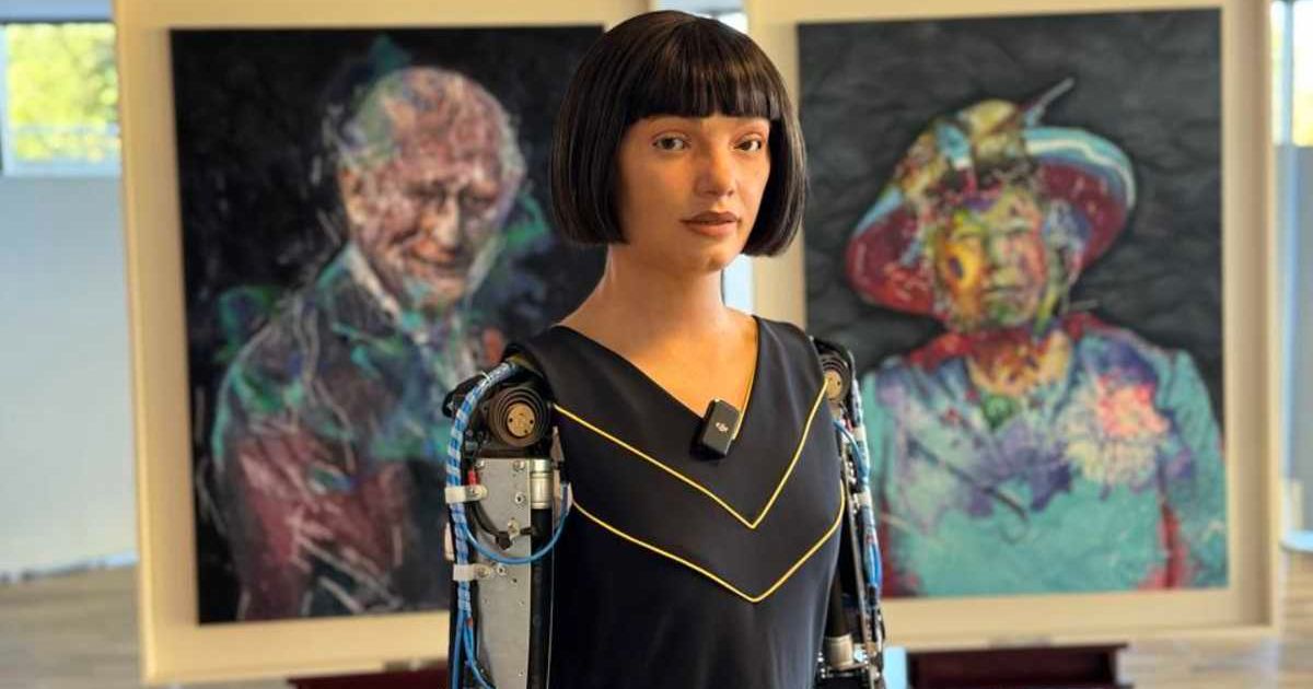 Robot Ai-Da stands in front of her portraits of King Charles and Queen Elizabeth. (Image Source: Website| Ai-Da Robot Studios)